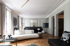a open layout with parquet floors, a white sofa and a black loveseat and ottoman, coffee tables and a creatie chandelier