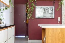 a pretty kitchen with an accent burgundy wall, white cabinets, a stained kitchen island and lots of planted greenery