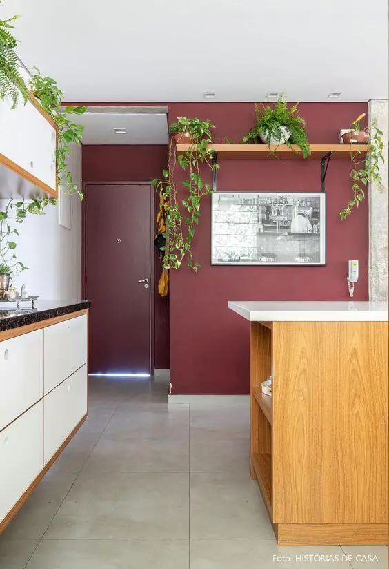 a pretty kitchen with an accent burgundy wall, white cabinets, a stained kitchen island and lots of planted greenery