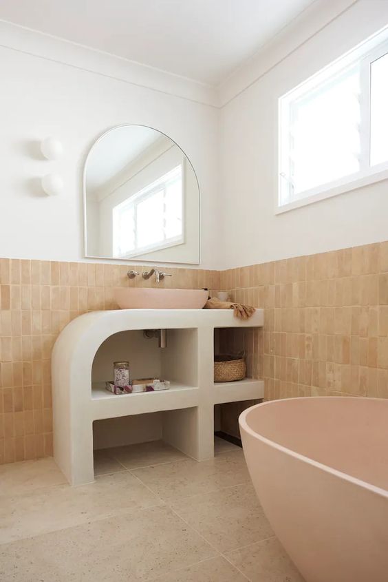 a quirky modern bathroom done with stoen and terracotta tiles, a pink tub, a curved vanity and a pink sink