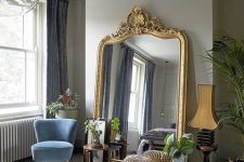 a refined Parisian bedroom with colorful furniture, grey walls, an oversized mirror in a gilded frame and a bubble chandelier
