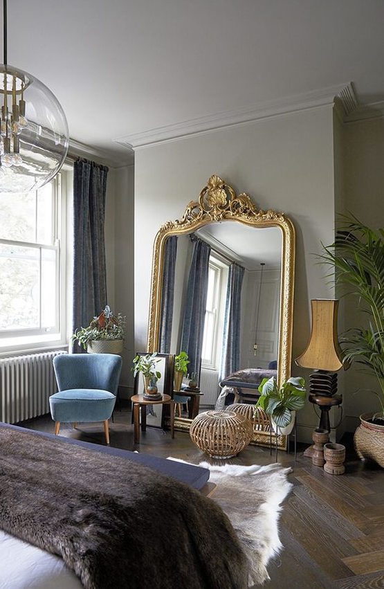 a refined Parisian bedroom with colorful furniture, grey walls, an oversized mirror in a gilded frame and a bubble chandelier