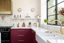 a refined burgundy kitchen with white stone countertops and a backsplash, a gold hood and open shelves is wow