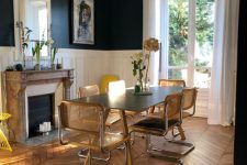 a refined dining room with black walls and paneling, a chevron floor, a fireplace, a table and cane chairs, some blooms