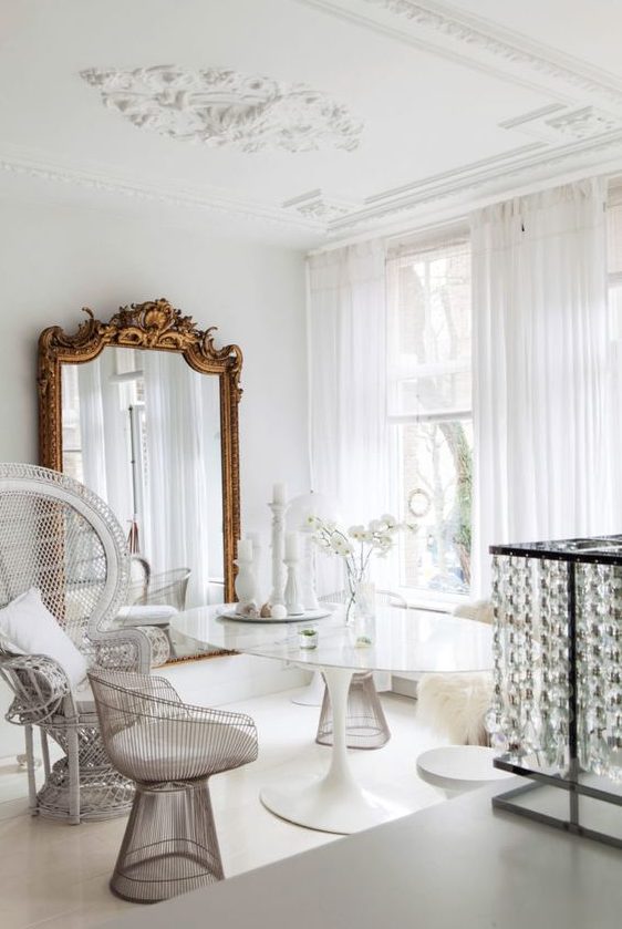 a refined dining space with a glass table, catchy and mismatching chairs, a huge mirror in a refined gilded frame