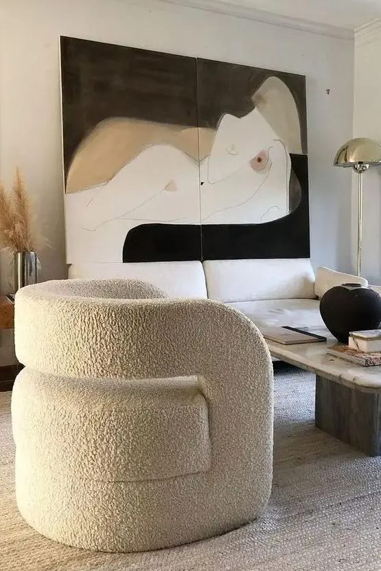 a refined living room with a creamy sofa, a coffee table, a curved chair, a statement artwork and pampas grass