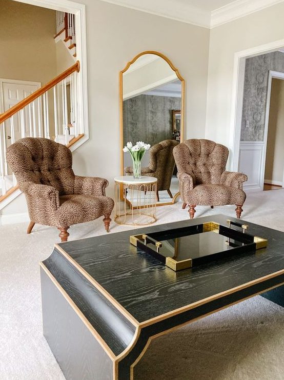 a refined living room with a statement mirror in a gilded frame, vintage leopard print chairs, a dark coffee table that echoes with the mirror in its shape