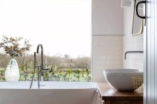 a refined modern bathroom with a glazed wall to enjoy the views, a tub, a terracotta tile floor, a vanity and a sink