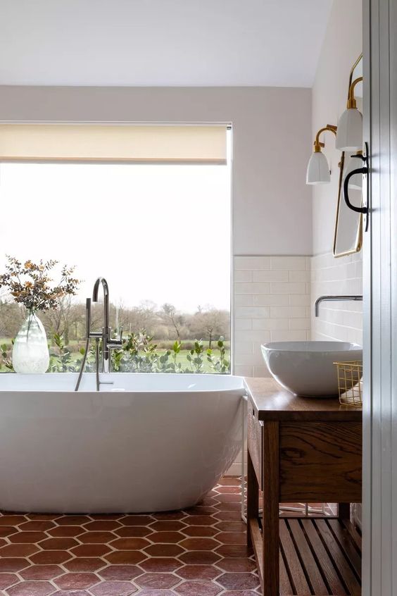 a refined modern bathroom with a glazed wall to enjoy the views, a tub, a terracotta tile floor, a vanity and a sink