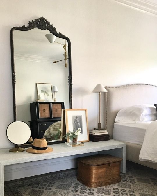 a refined neutral bedroom with a bench with decor and an oversized mirror in a black ornated frame