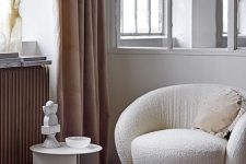 a refined nook with a white boucle chair, a pillow, a side table, some lovely decor and beige curtains