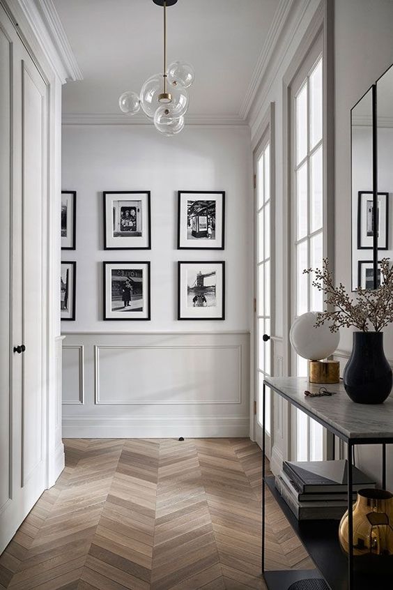 a refined space with paneling, a chevron floor, a console table, a black and white gallery wall and a mirror