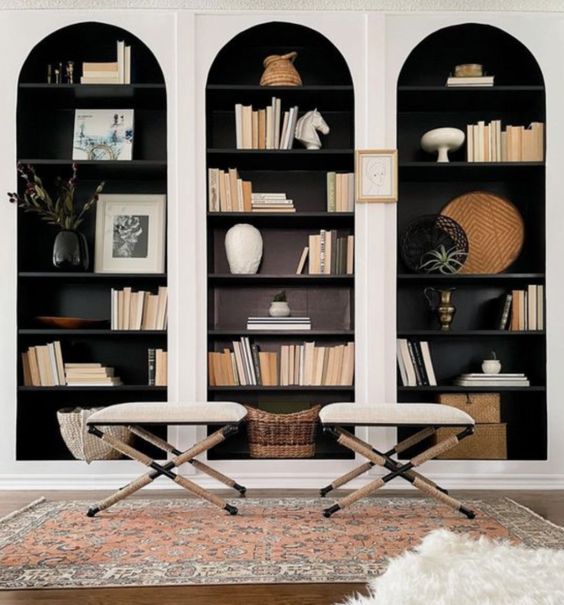 a refined space with white arched bookcases and black shelves and backing, creamy folding stools and a boho rug