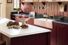 a refined vintage kitchen with burgundy cabinets and a beadboard backsplash, black and white countertops and vintage fixtures