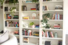 a row of arched bookcases with books, greenery, a creamy sofa with pillows and a side table for a living room