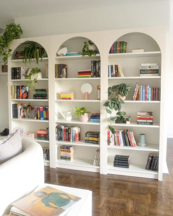 a row of arched bookcases with books, greenery, a creamy sofa with pillows and a side table for a living room