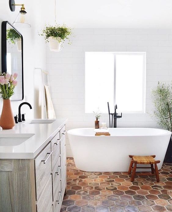 a serene bathroom with white walls, an oval tub, a terracotta hex tile floor, a reclaimed wood vanity and greenery