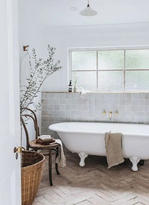a serene neutral bathroom with grey Zellige tiles and a parquet floor, a clawfoot tub, a wooden chair, a basjet and some delicate decor
