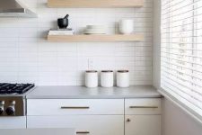 a serene white kitchen with a stacked tile wall, creamy cabinets, open shelves and brass fixtures for more chic