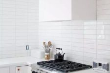 a serene white kitchen with a white stacked tile backsplash, copper fixtures and a white hood is very welcoming