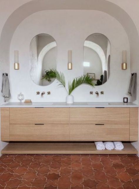 a sink space with an arched niche, a vanity, mirrors, a terracotta tile floor and chic gold wall sconces
