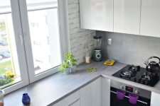a small and minimalist white kitchen with grey countertops and a countertop as a windowsill table plus black stools
