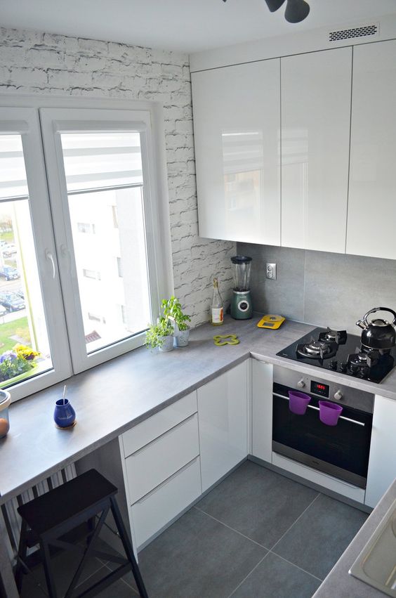 a small and minimalist white kitchen with grey countertops and a countertop as a windowsill table plus black stools