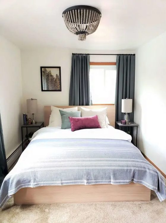 A small and narrow bedroom with a light stained bed and neutral bedding, nightstands with lamps and a beaded chandelier