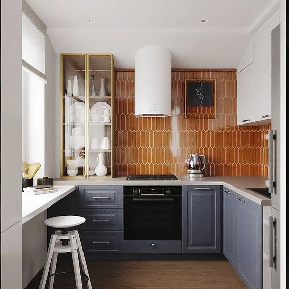 a small grey and white kitchen with an orange tile backsplash, a glass cabinet and a windowsill as a table to have breakfasts here