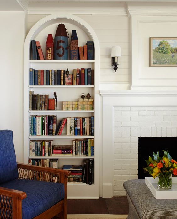 a small nook with a fireplace, an arched bookcase, a navy chair and an ottoman is a cool space for reading