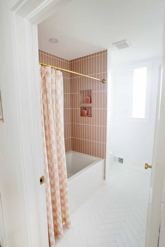 a small white bathroom with a bath space clad with terracotta tiles, white herringbone on the floor and white appliances