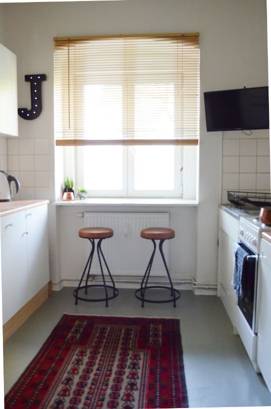 a small white kitchen with a windowsill used as a breakfast bar, with some simple decor and a bold rug