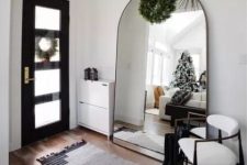 a small yet eye-catchy entryway with a large arched mirror, a whiet shoes cabinet, a rug and a chair