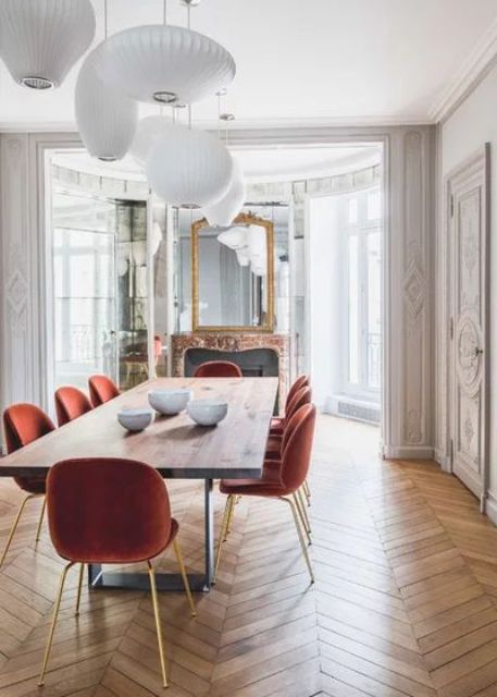 a sophisticated French dining room with a bay window, a fireplace, a chevron parquet floor, rust chairs and pendant lamps