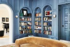a sophisticated living room with blue arched bookcases and shelves, a yellow curved sofa, a printed rug and a coffee table with decor