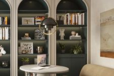 a sophisticated space with arched bookcases, dark green shelves and cabinets, books and lovely decor, a tan sofa and a round coffee table