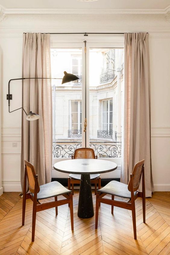 a stylish and chic dining nook at the window, a table, cane chairs, a black lamp and a chevron floor that adds elegance