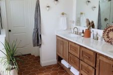 a stylish and cozy bathroom with white walls and a terracotta hex tile floor, a stained vanity, greenery and a large mirror