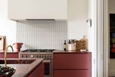 a stylish contemporary kitchen with lower burgundy cabinets and a large white hood, a skinny tile backsplash and burgundy stone countertops