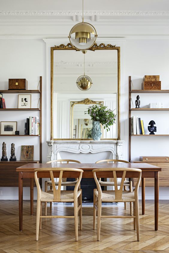 a stylish modern dining room with open shelves and cabinets, a non-working fireplace, a large mirror, a table and chic chairs