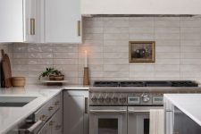 a stylish two-tone kitchen with a white stone countertops and a stacked tile backsplash plus brass fixtures