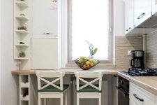 a tiny white L-shaped kitchen with butcherblock countertops, a windowsill table and white stools plus shelves