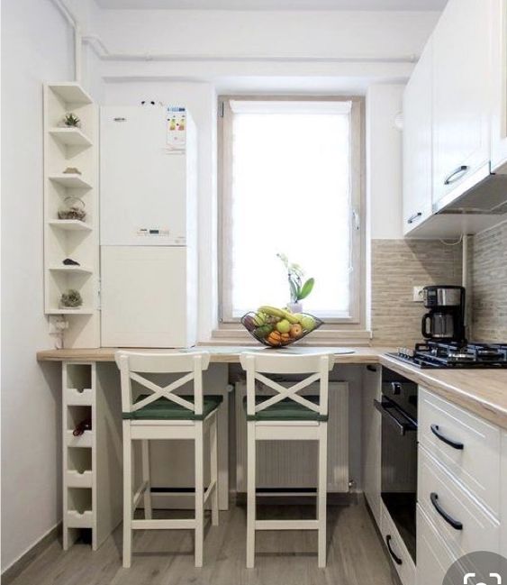 A tiny white L shaped kitchen with butcherblock countertops, a windowsill table and white stools plus shelves