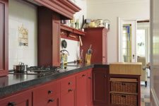 a vintage burgundy kitchen with black countertops and a tile backsplash plus black fixtures and basket drawers