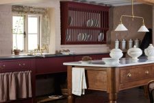 a vintage burgundy kitchen with black countertops, wooden beams and a matching stained kitchen island, some lamps