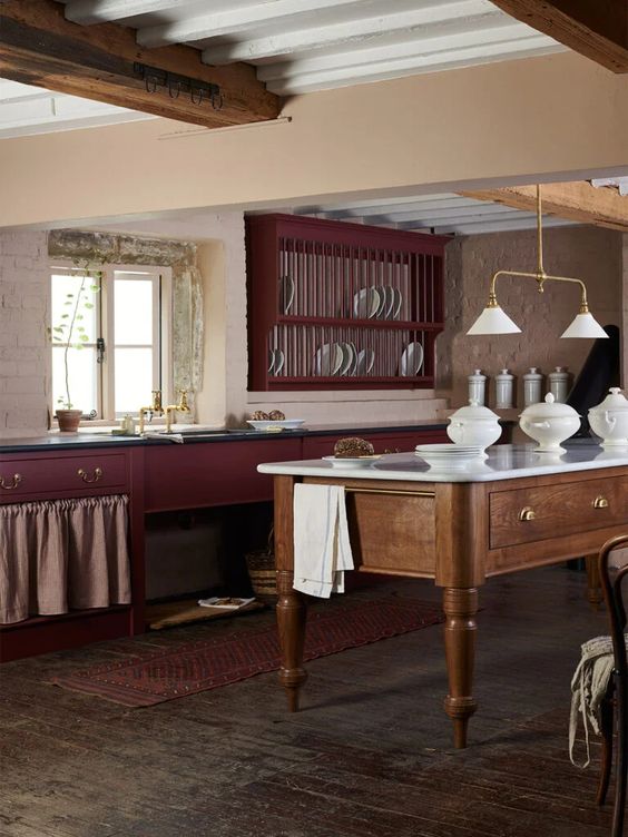 a vintage burgundy kitchen with black countertops, wooden beams and a matching stained kitchen island, some lamps