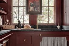 a vintage burgundy kitchen with match walls, black stone countertops and gold fixtures plus a vintage artwork