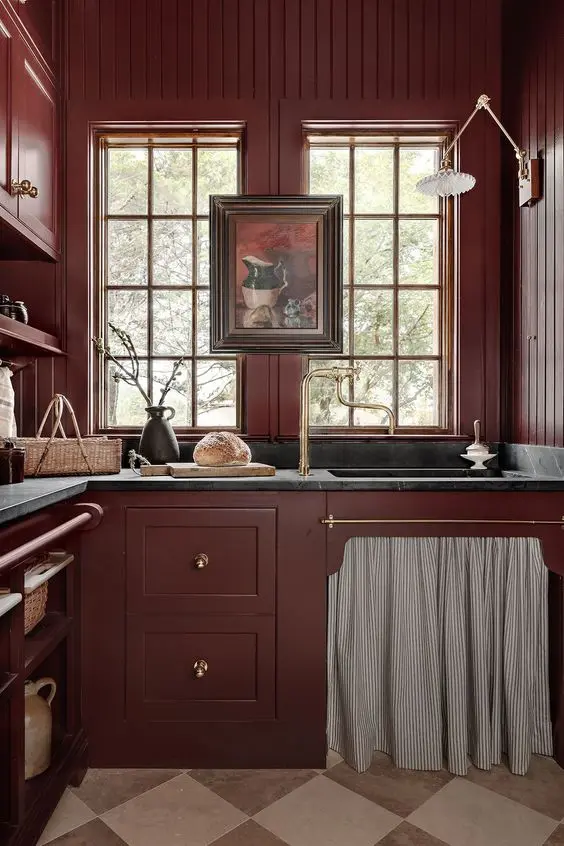 a vintage burgundy kitchen with match walls, black stone countertops and gold fixtures plus a vintage artwork