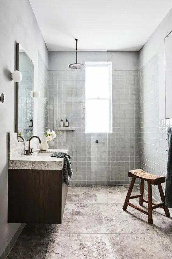 A wabi sabi bathroom with grey square tiles and large format stone tiles, a floating vanity, a stained wooden stool and a mirror