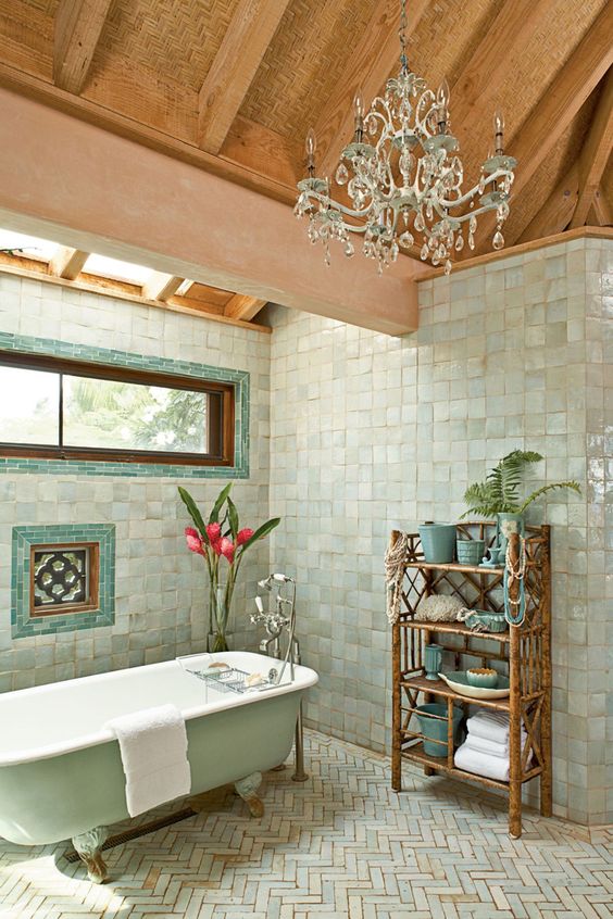 a whimsical bathroom clad with Zellige square and herringbone tiles, a mint tub, a skylight and window, a chic chandelier